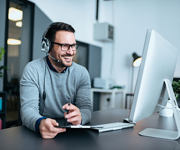 Mann mit Headset lächelnd vor einem Computer
